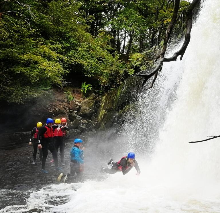 Group of adults with instructors jumping into a waterfall.